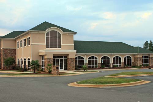 Parking lot view of beige siding commerical building with green roof.